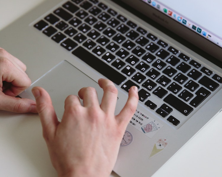a laptop with a pair of hands scrolling with the trackpad